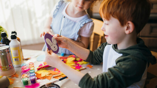 Two children painting and drawing easter arts and crafts at home.