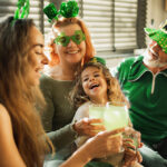 Happy smiling family ready for St. Patrick's day party. People wearing green clothes, green hats, deely bobber, and glasses with clover shaped. Family drinking green non alkohol soda water and celebrating Saint Patrick's Day.