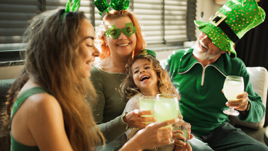 Happy smiling family ready for St. Patrick's day party. People wearing green clothes, green hats, deely bobber, and glasses with clover shaped. Family drinking green non alkohol soda water and celebrating Saint Patrick's Day.
