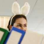 Young woman wearing bunny ears in office, folders in foreground