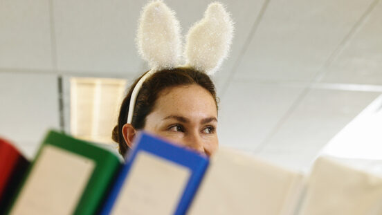 Young woman wearing bunny ears in office, folders in foreground