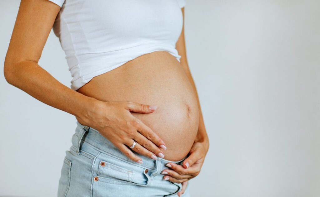 Pregnant woman's body in white shirt and jeans posing on white background. 
