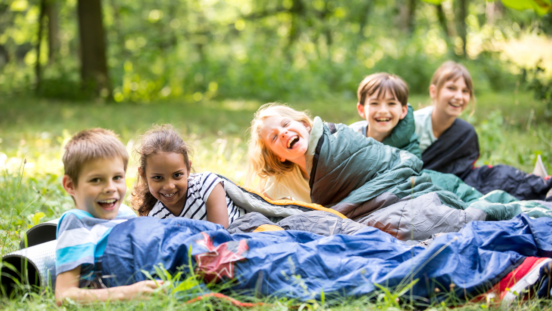 Group of young kids in sleeping bags lying on the grass