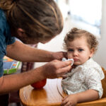 Dad wipes his toddler's face while she sits in her high chair