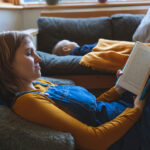 Woman reading book in living room with little son sleeping