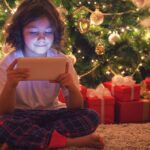 Child on a smart tablet in front of a Christmas tree