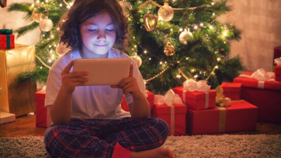 Child on a smart tablet in front of a Christmas tree