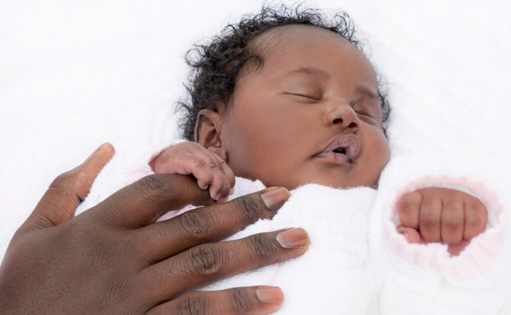 Sleeping African American baby clutches mother's finger.