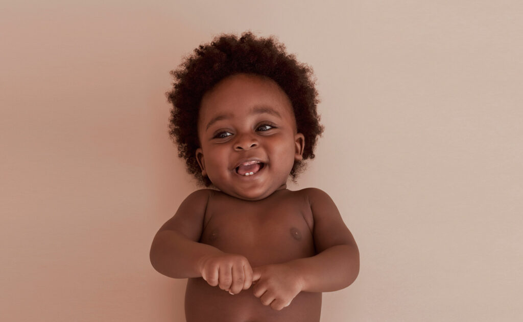 Curly haired African American infant smiles at camera.