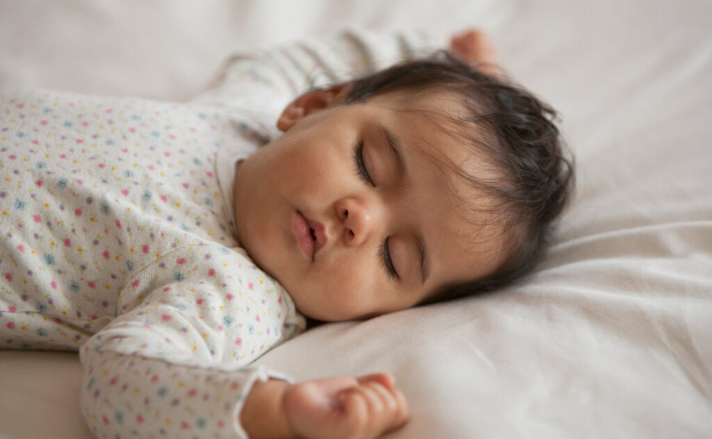 Sleeping infant with dark hair reeling in bed.