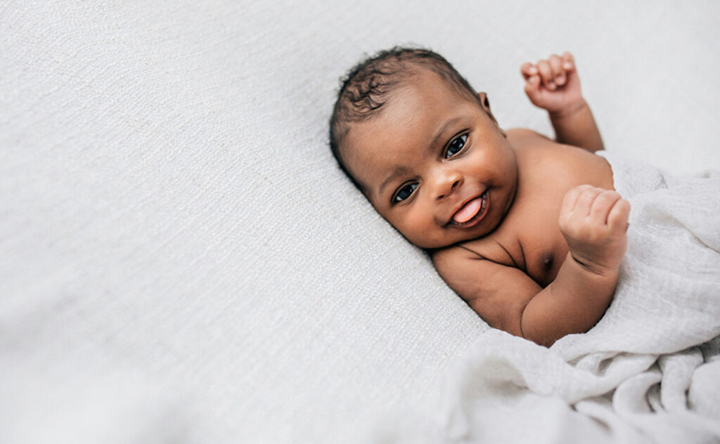 Cute African American newborn looks towards camera with tongue poking out.