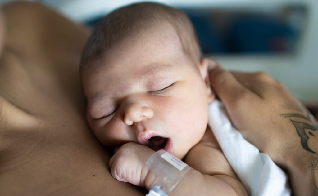 Sleeping newborn with hospital identity bracelet sleeps up on mother's chest.