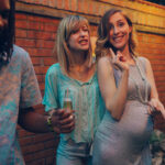 Pregnant woman and friends having fun together at garden party. Dancing and drinking. Selective focus to pregnant woman looking at camera.