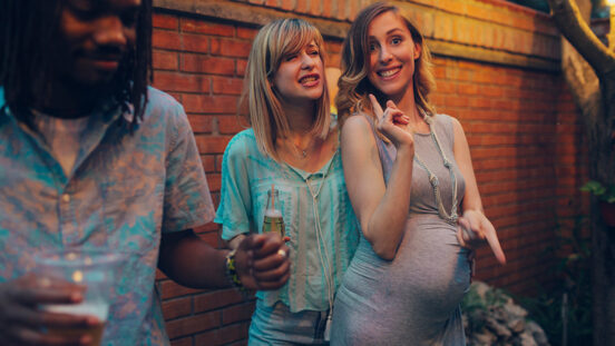 Pregnant woman and friends having fun together at garden party. Dancing and drinking. Selective focus to pregnant woman looking at camera.