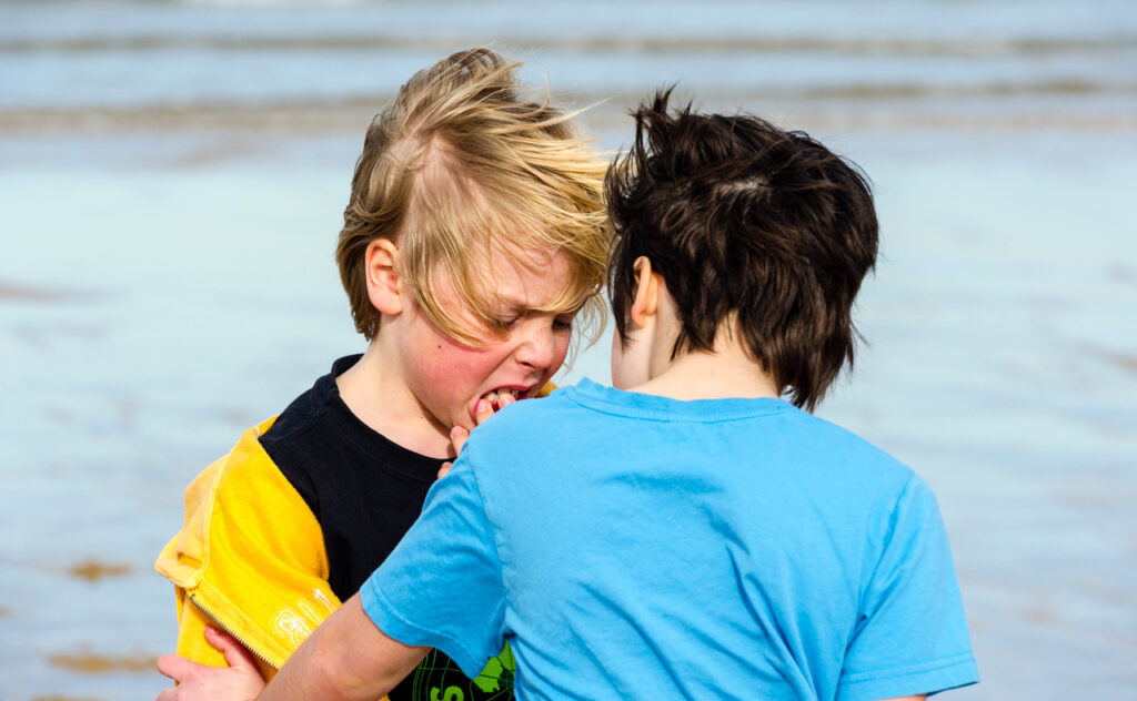 A girl comforts her friend who hurt his mouth playing on the beach. - stock photo