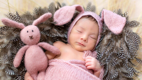 Sleeping newborn in lavender coloured woollen bunny ear bonnet and blanket.