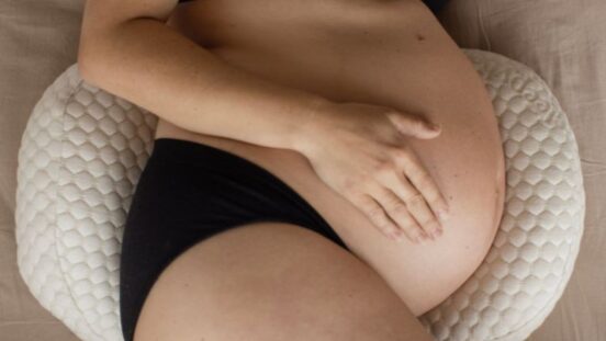 Side view of woman's pregnant belly lying down on a supportive cushion