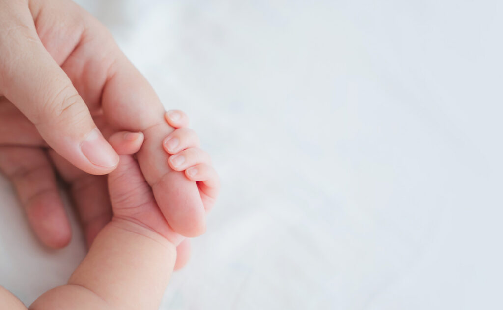 Newborn hand clutching an adult finger.