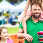 Father with two kids at an outdoor summer carnival festival fair or amusement park, family fun