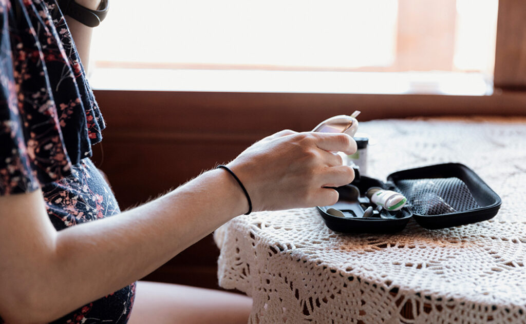 Pregnant woman testing blood sugar at home. She's puncturing her finger.