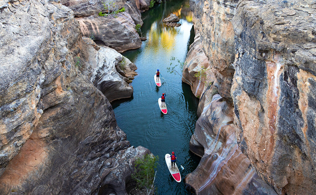 An arial view of three stand up paddleboarders in Cobbold Gorge in North West Queensland.