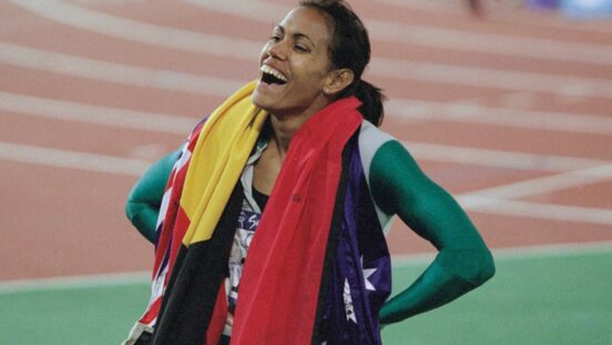Cathy Freeman, the Australian flag and the Australian Aboriginal flag draped around her shoulders, after winning the women's 400 metres event of the 2000 Summer Olympics