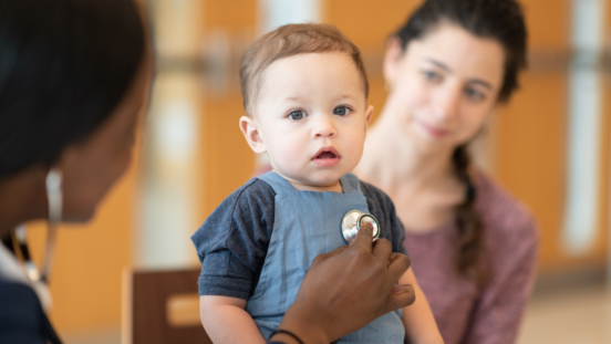 Cute toddler boy with his mouth open, looking at the camera as a doctor's hand put a stethoscope to his chest