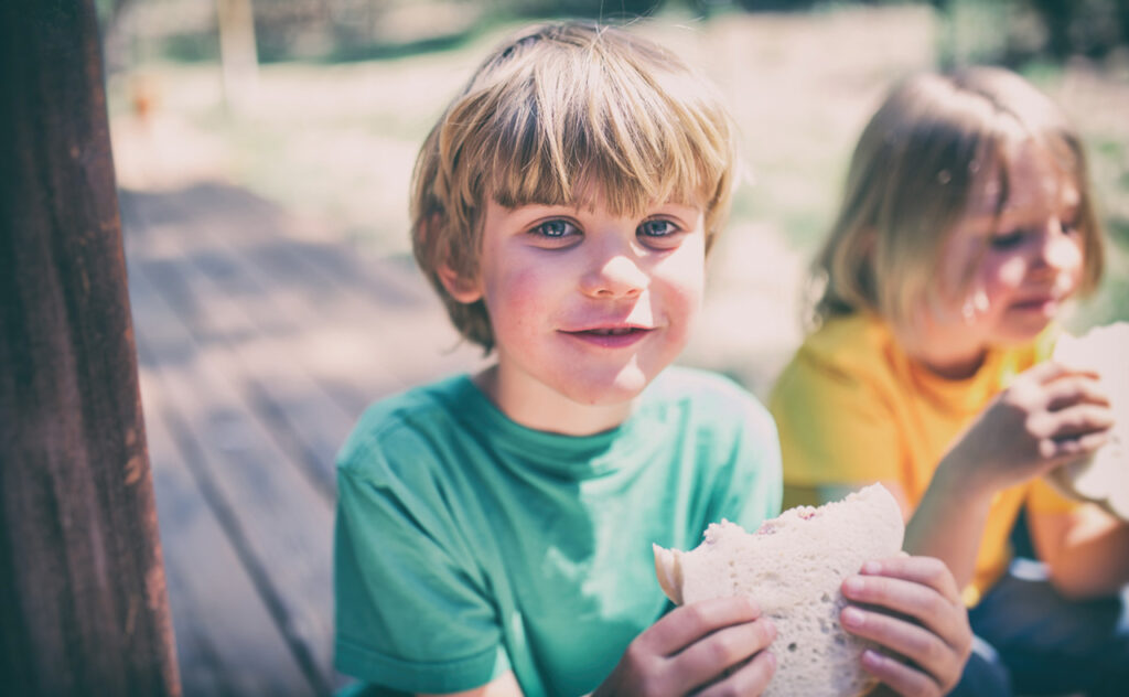 Children eating sandwiches on a porch step outside.