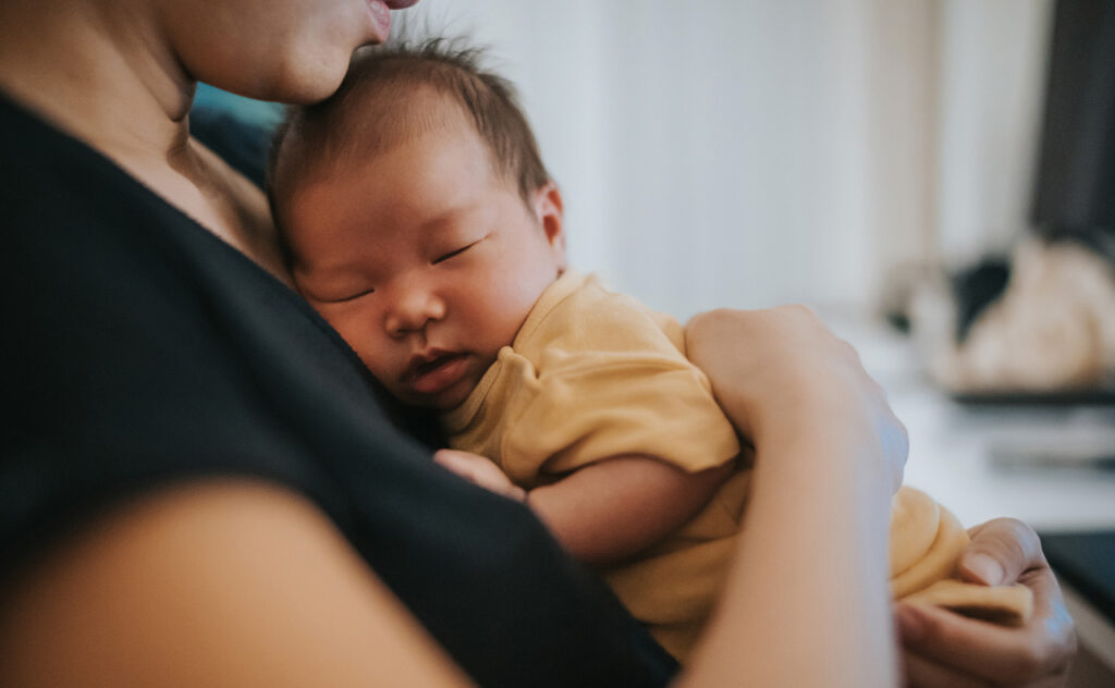 Dark haired baby sleeping upright on mother's chest