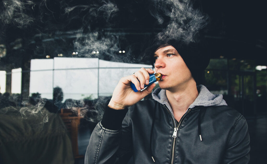 Vape steamer urban youngster casual look in outdoor cafe 