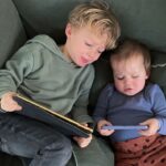 Young boy and toddler boy sitting on lounge looking at screens