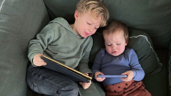 Young boy and toddler boy sitting on lounge looking at screens