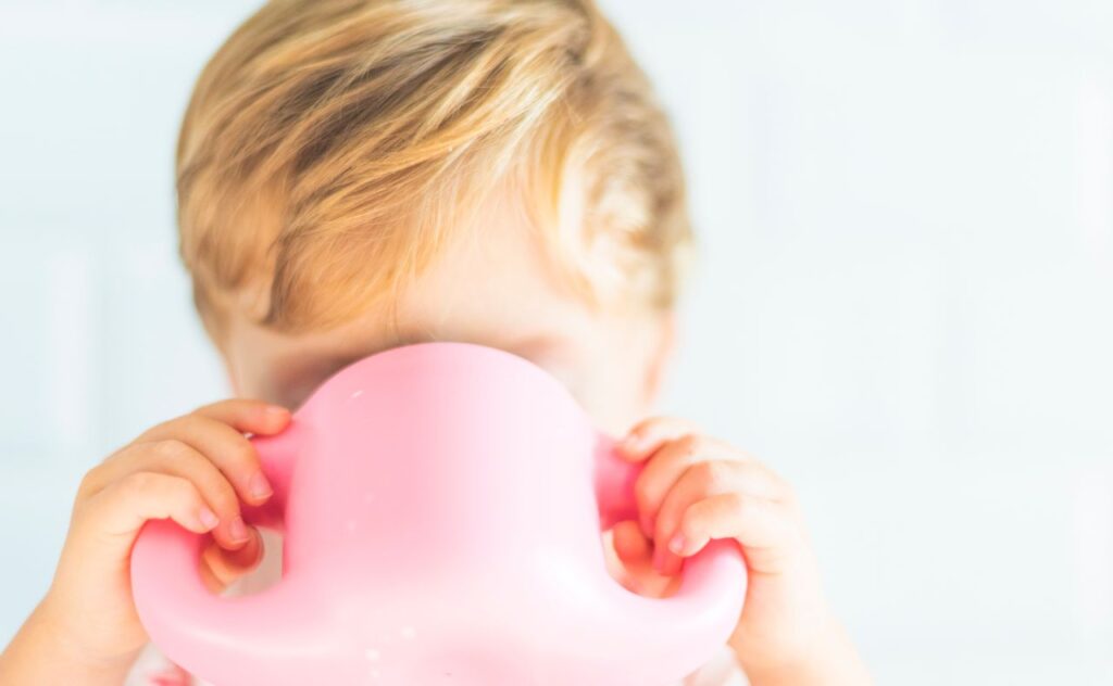 Blonde haired children drinking from a two-handled large pink cup