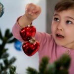 Little girl hanging 2 red heard baubles on Christmas tree