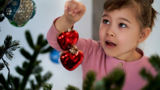 Little girl hanging 2 red heard baubles on Christmas tree
