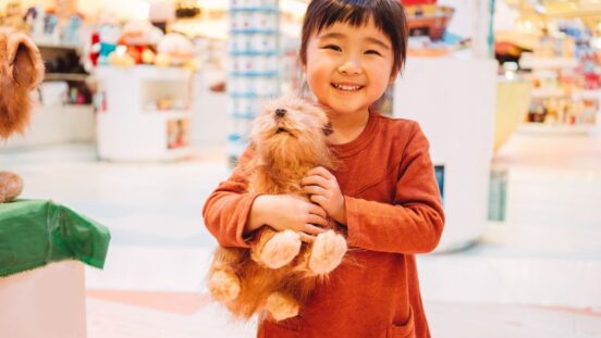 Smiling little Asian girl in a toy store holds a cuddly toy dog