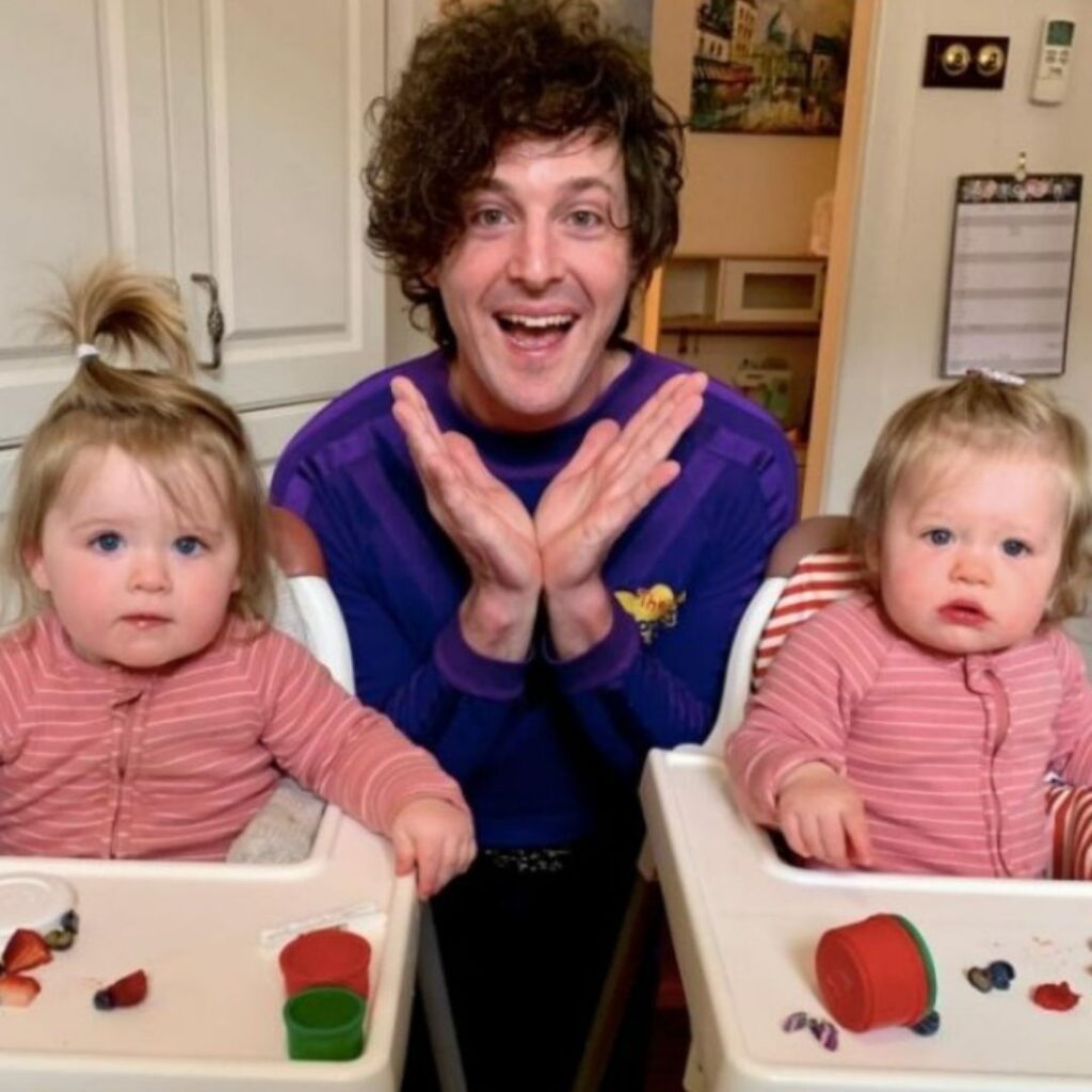 Lachy Gillespie dressed in his purple Lachy Wiggle costume with his daughters who are sitting in their high chairs