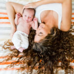 Stylised portrait of mother with curly hair holding newborn baby.