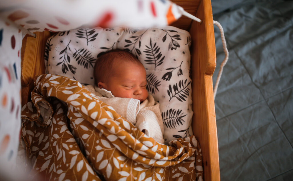 Newborn baby sleeps in wooden hanging retro cradle with muslin diapers. Top view.