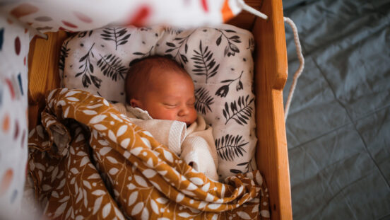 Newborn baby sleeps in wooden hanging retro cradle with muslin diapers. Top view.