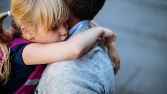 Blonde toddler girl looks upset and has arms around her dad's neck