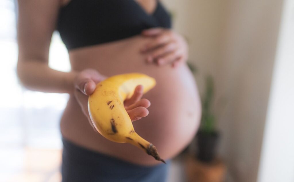 Pregnant woman in profile, blurred out, holding out a banana