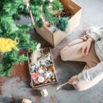 Boy sitting on floor with Christmas decorations. box decorate Christmas tree, top view