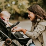 A smiling mother with her child in a stroller in a park.