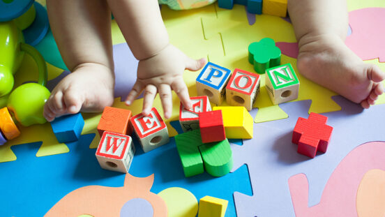 Small toddler hand reaching for alphabet blocks on colourful background.