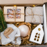 Christmas gift basket with wax candle, ceramic house, paper box with candy, cozy socks and bath bomb.