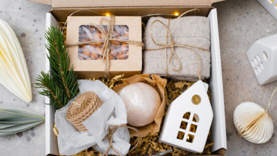 Christmas gift basket with wax candle, ceramic house, paper box with candy, cozy socks and bath bomb.