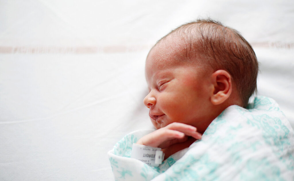 Side profile of a newborn wrapped in a hospital blanket at maternity ward.
