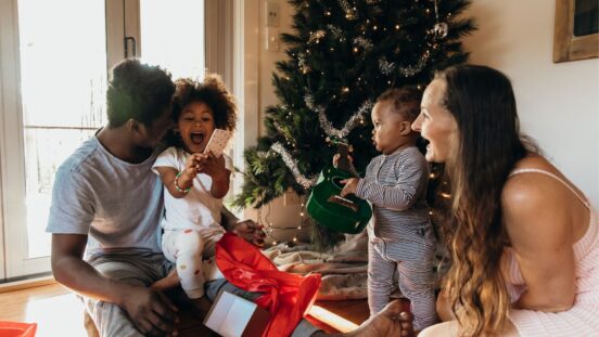 Real life young Australian multi-ethnic family enjoys relaxed time together by the tree in their pyjamas on Christmas morning