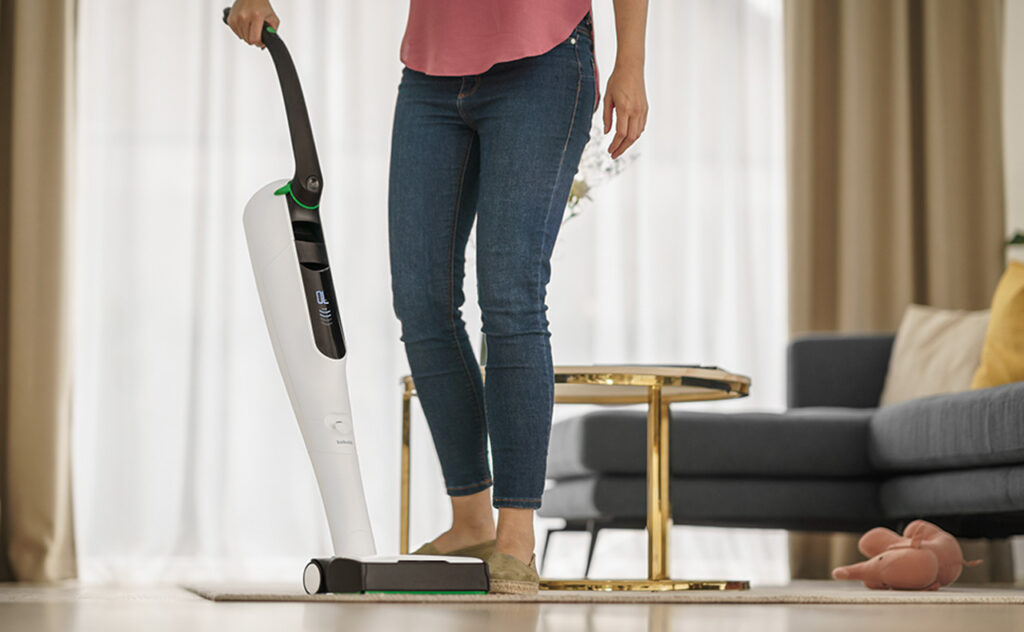 Woman uses Thermomix Kobold cordless vac in modern living area.